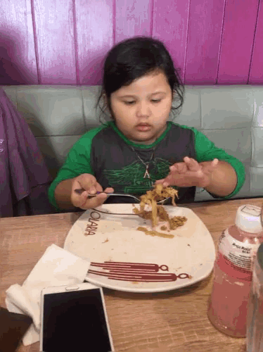 a little girl sitting at a table with a plate that says o'lana