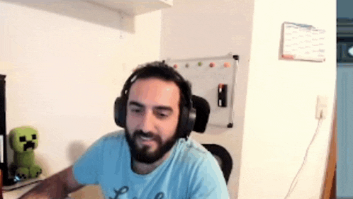 a man with a beard wearing headphones is sitting at a desk in front of a white board .