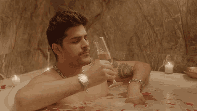 a man in a bathtub holds a glass of champagne