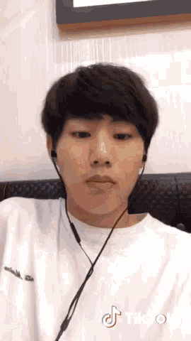 a young man wearing ear buds and a white shirt has a tiktok sticker on his face