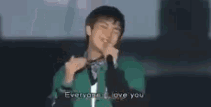 a man in a green jacket is singing into a microphone while making a heart shape with his hands .