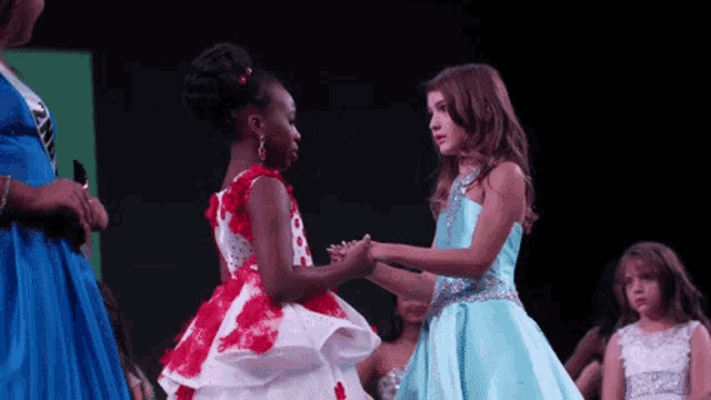 a girl in a blue dress is shaking hands with a girl in a red and white dress