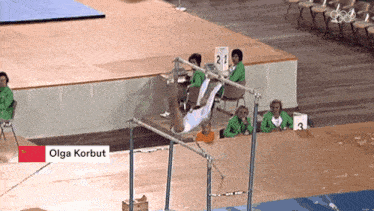 a gymnast is doing a trick on a bar and the name olga korbut is on the bottom