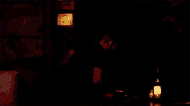 a man is standing in a dark room next to a bottle of wine and a candle .
