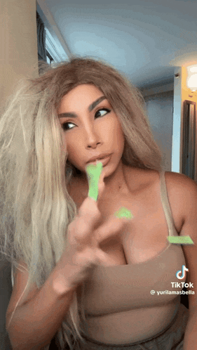 a woman with long blonde hair is holding a green object in her mouth ..