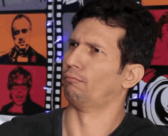 a man is making a funny face in front of a wall with pictures of people on it