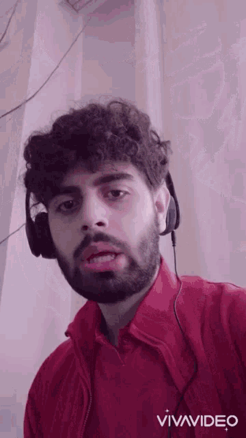 a man with a beard wearing headphones and a red jacket is being filmed by vivavideo