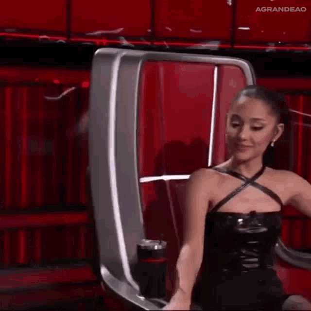 ariana grande is sitting in a chair on the voice with a cup of coffee in her hand .