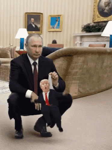 a man in a suit and tie is squatting down next to a trump puppet