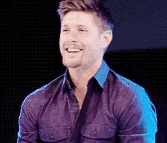 a man in a purple shirt is smiling and laughing .
