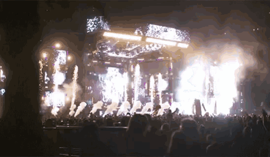 a crowd of people watching a concert with fireworks coming out of the stage