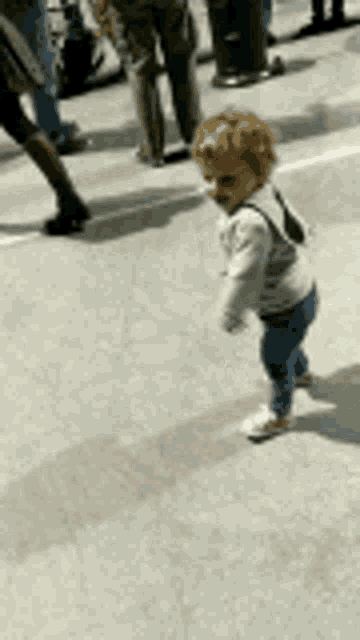 a baby is walking across a street in front of people .