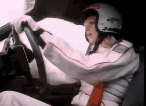 a man wearing a helmet and a white jacket is driving a car