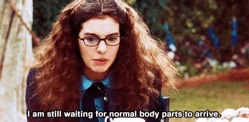 a woman wearing glasses is sitting in a chair and says i am still waiting for normal body parts to arrive .