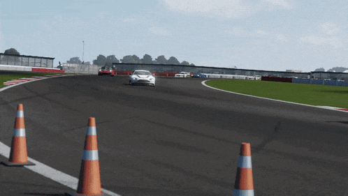 a white car is driving down a race track with orange and white cones