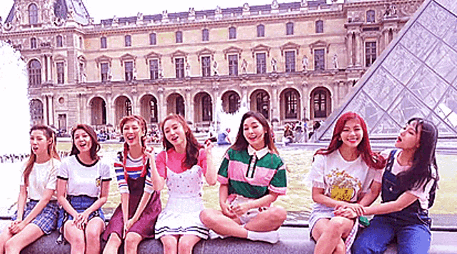 a group of girls are sitting on a wall in front of a fountain .