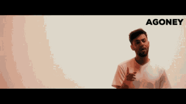 a man in a white shirt is standing in front of a white wall with agoney written on it