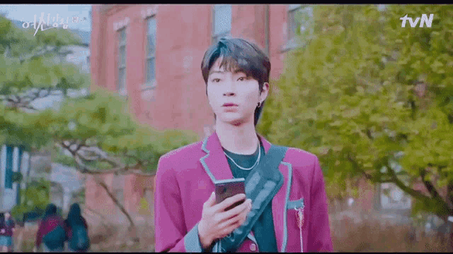 a young man in a purple suit is holding a cell phone .