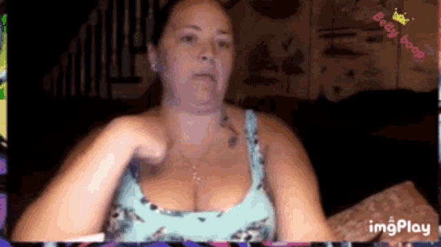 a woman in a blue tank top is sitting on a couch and making a funny face .