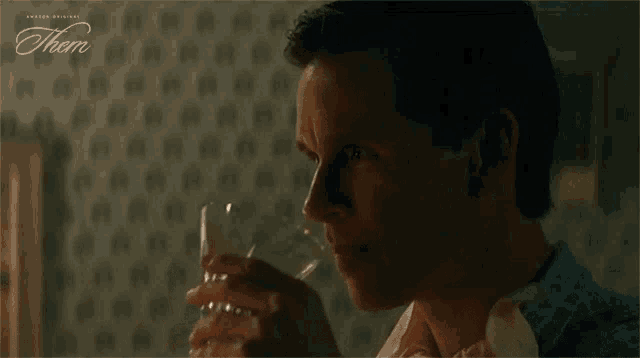 a man is drinking a glass of whiskey in front of a wall with polka dots .