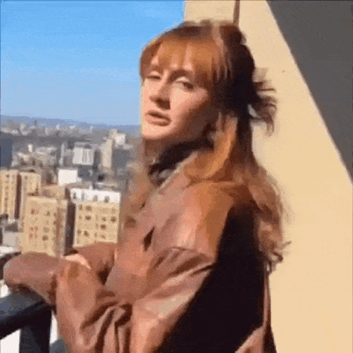 a woman with red hair is standing on a balcony with a view of a city .