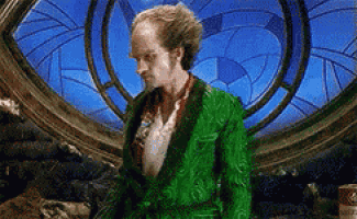 a bald man in a green robe is standing in front of a stained glass window .