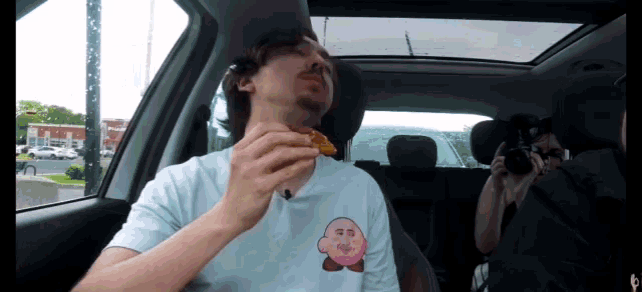 a man in a car wearing a kirby shirt eating a pizza