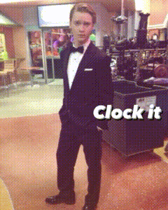 a man in a tuxedo is standing in front of a sign that says clock it on it