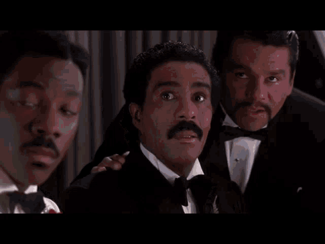 a man in a white tuxedo and bow tie has a red rose in his pocket