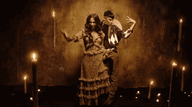 a man and a woman are dancing in a dark room surrounded by candles