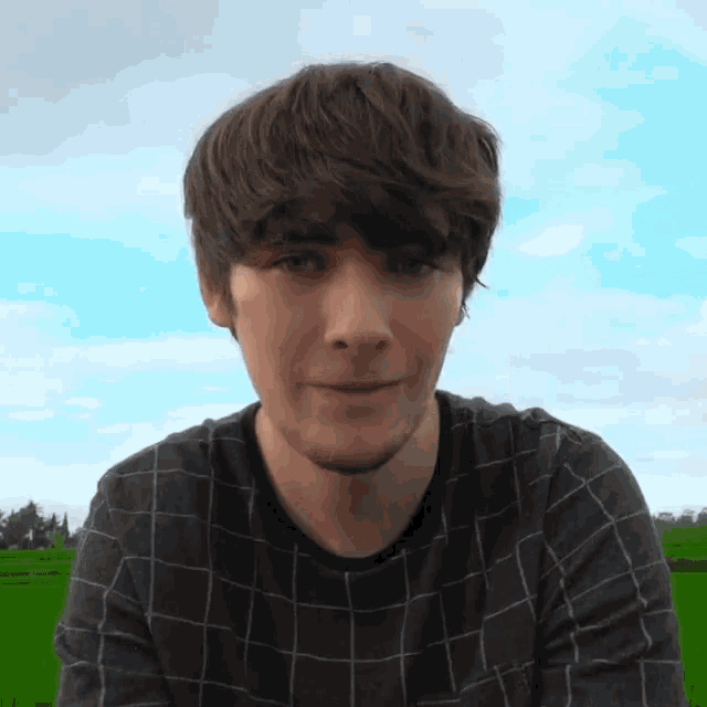 a young man in a plaid shirt is smiling in front of a green field