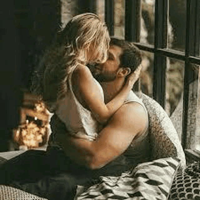 a man and a woman are kissing while sitting on a couch in front of a window .