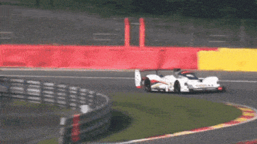 a race car is going around a curve on a track with a red barrier in the background