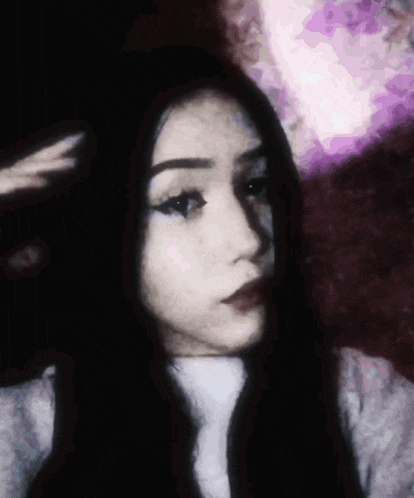 a girl with long black hair looks at the camera with her hand on her head