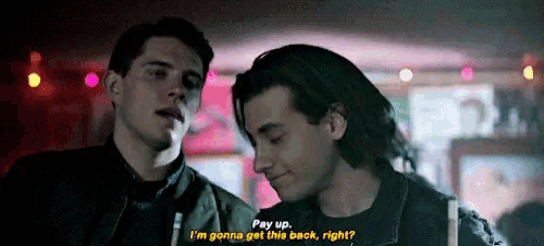 two young men are standing next to each other and one of them is saying pay up .