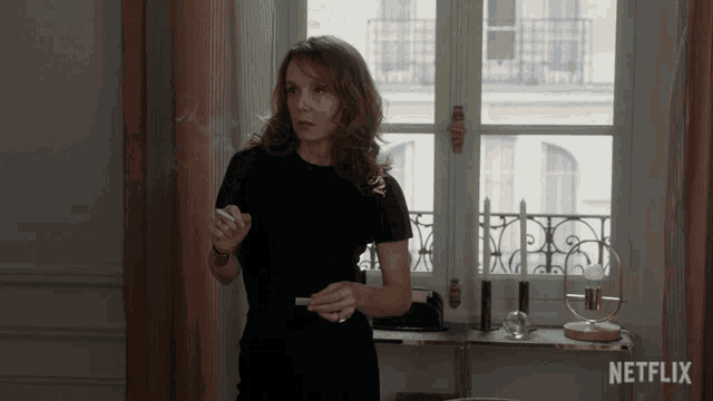 a woman in a black dress stands in front of a window with a netflix logo on the bottom