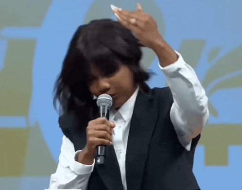 a woman in a black jacket and white shirt is holding a microphone and adjusting her hair .