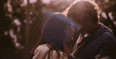 a man and a woman are kissing in front of some trees