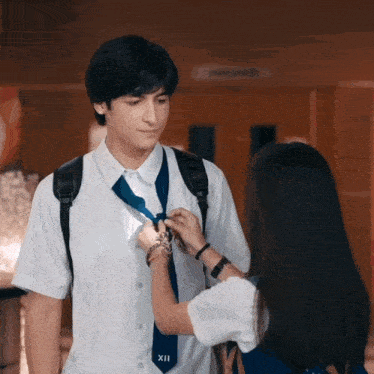 a girl adjusts a boy 's tie which has the number xii on it