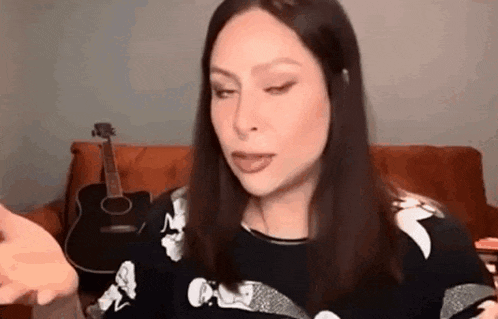 a woman is sitting on a couch with a guitar in the background and making a funny face .