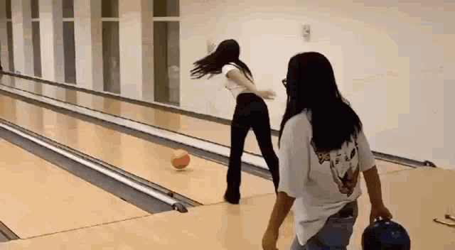 two women are bowling on a bowling alley and one of them is holding a bowling ball .