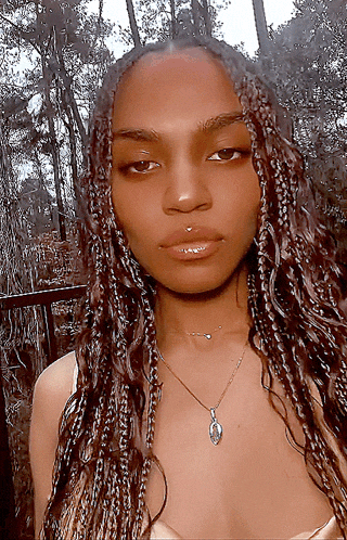 a woman with braids is wearing a necklace with a pendant