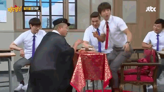 a group of men are sitting around a table in a classroom with a sign that says jtbc on it