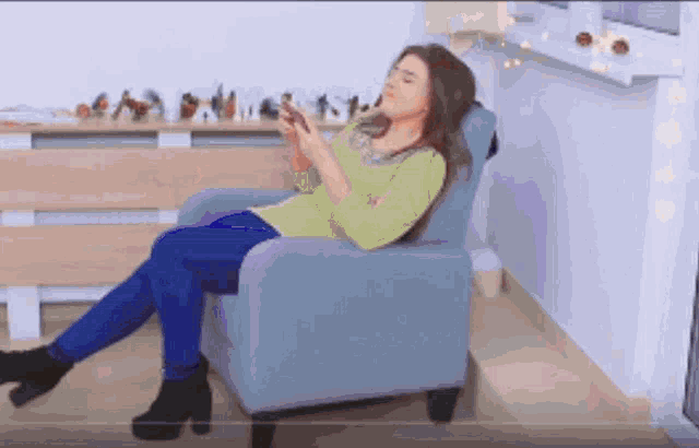 a woman is sitting in a chair and looking at her phone