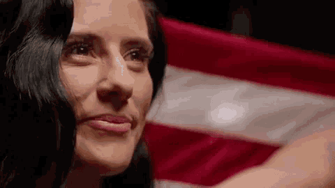 a close up of a woman 's face with an american flag in the background .