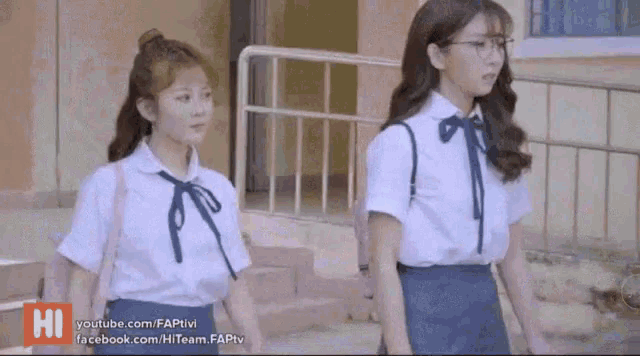 two girls in school uniforms are standing next to each other on a sidewalk .