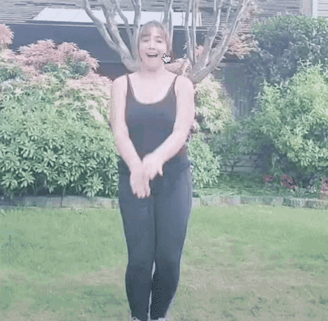 a woman in a black tank top and black leggings is standing in a grassy yard