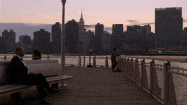 a man sits on a bench with a view of the city skyline behind him