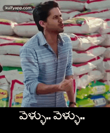 a man in a striped shirt is standing in front of a pile of rice bags .