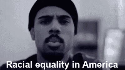 a black and white photo of a man with a beard wearing a beanie and talking about racial equality in america .